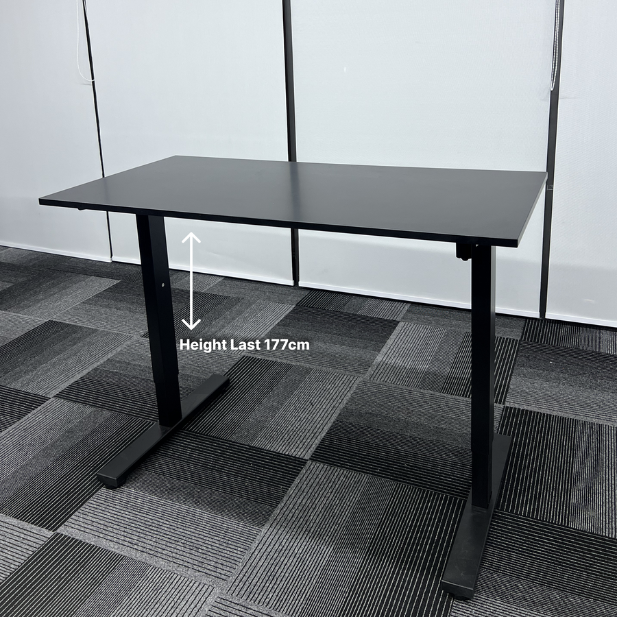 Black adjustable desk on a checkered floor with height measurement text.
