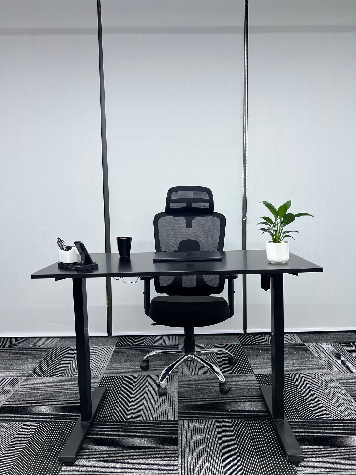 Modern office setup with a black desk, chair, and decor items against a gray wall.