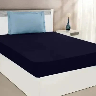 Navy blue fitted sheet on a bed with a white headboard and blue pillow.