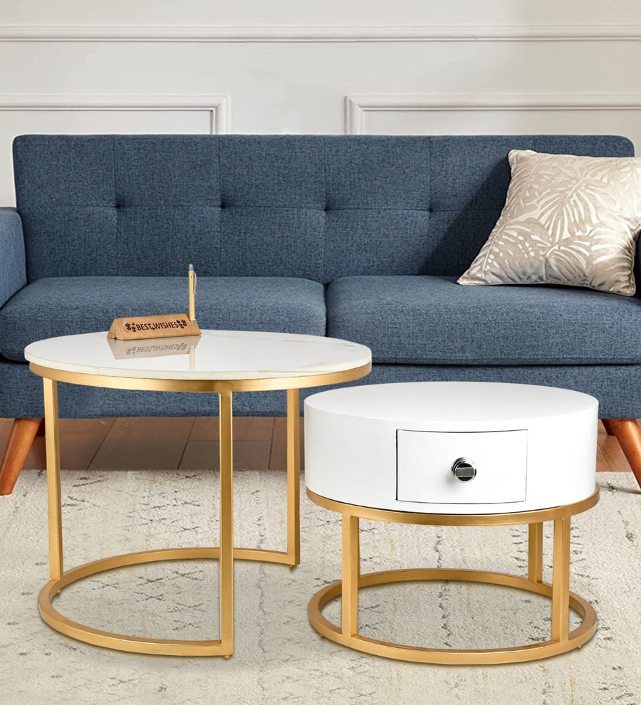Round coffee table with gold legs and white marble top next to a blue sofa with a white ottoman.
